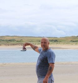 Optical illusion of mature man holding boat on sea at beach