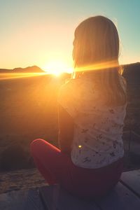 Woman sitting in park against sky during sunset