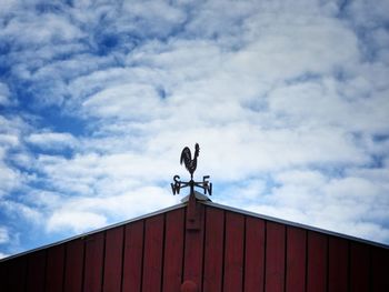 Low angle view of bird on building against cloudy sky