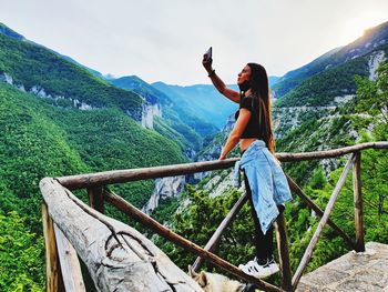 Full length of woman photographing with mobile phone against sky