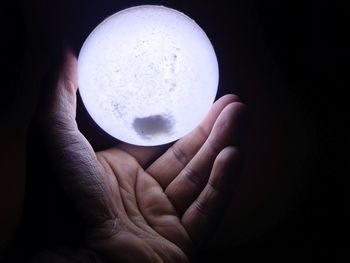Close-up of hand holding crystal ball against black background