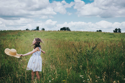 Teen girl twirling in a grassy field on a cloudy summer day