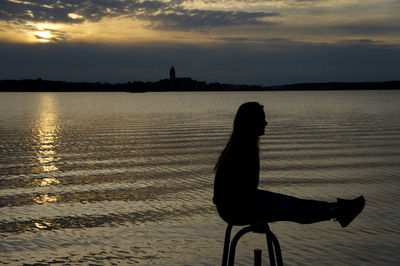 Silhouette man sitting by sea against sky during sunset