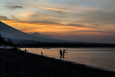 People on beach against sky during sunset