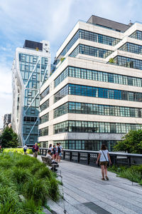 People walking by modern buildings in city against sky