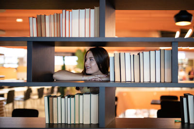 Smiling young woman leaning on bookshelf at library