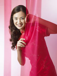 Portrait of smiling woman holding textile while standing against backdrop