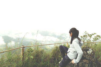 Side view of woman looking at railing against sky