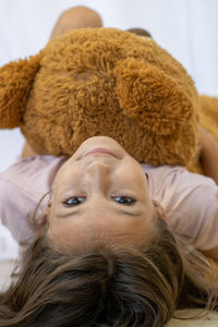 Portrait of girl holding teddy bear lying on bed