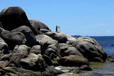 Man standing on rock by sea against clear sky