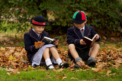 Full length of boy and girl reading books while sitting on grass