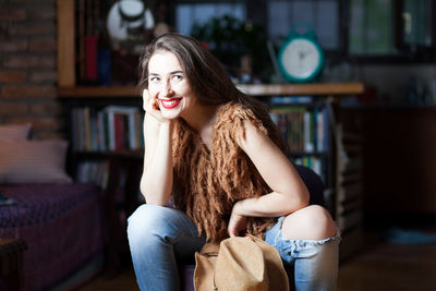 Portrait of smiling young woman with head in hand while sitting at home