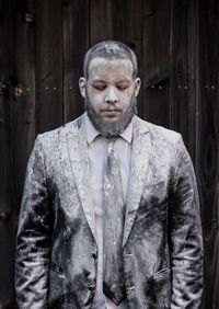 Man wearing suit covered in flour standing against wooden fence