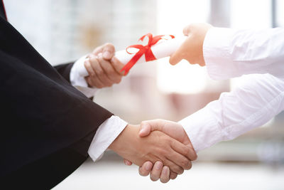 Midsection of man handshaking with student holding certificate