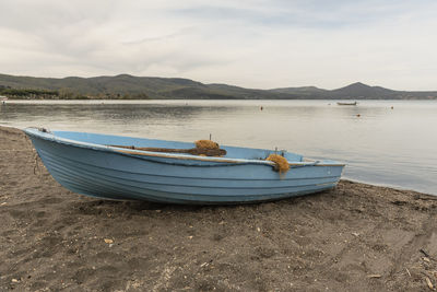 Boats moored on shore by lake against sky