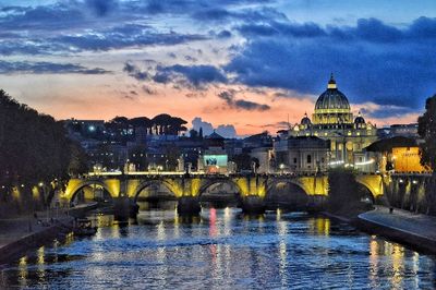 Bridge over river by buildings against sky at dusk