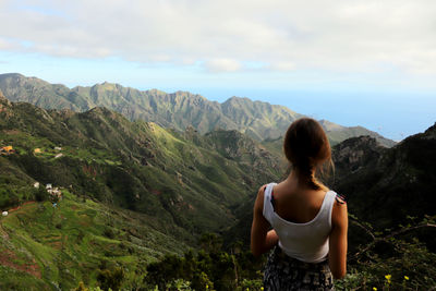 Rear view of woman standing on mountain against sky