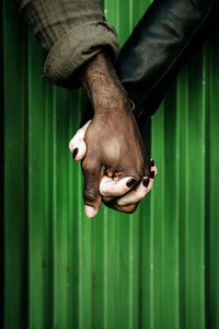 Cropped image of couple holding hands against green corrugated iron