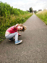 Portrait of cute girl gesturing while crouching on road against sky