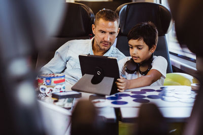 Mid adult man with son looking at digital tablet while sitting in passenger train