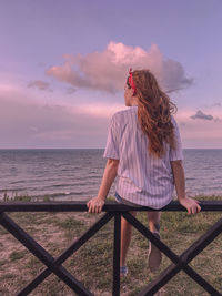 Woman standing by railing against sea during sunset