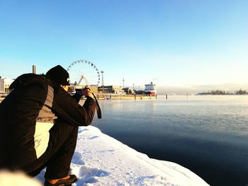 Man sitting on snow against sky