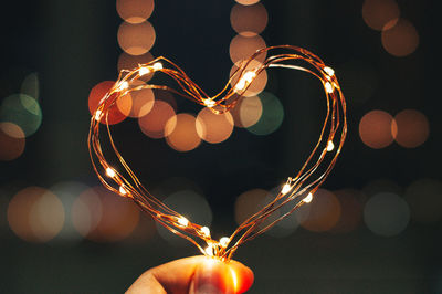 Cropped hand of woman holding illuminated string light in darkroom