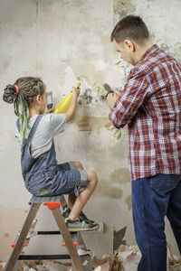 Side view of siblings standing against wall