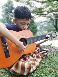 Cute boy playing guitar while sitting on grass