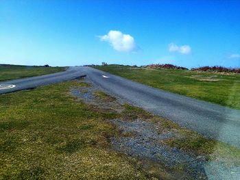 Road passing through field against cloudy sky