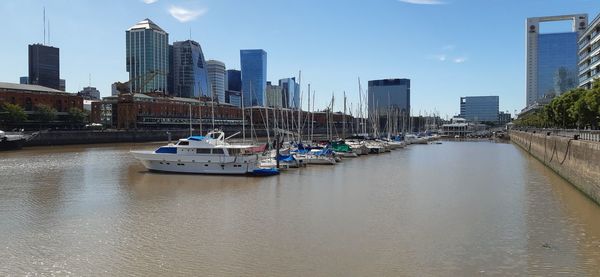 Boats in river by buildings in city against sky