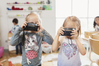 Little girls holding toy cameras in classroom