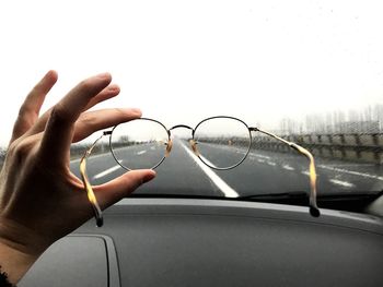 Cropped hand holding eyeglasses in front of car windshield