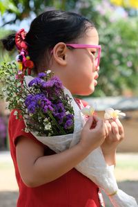 Cute girl holding bouquet while standing outdoors