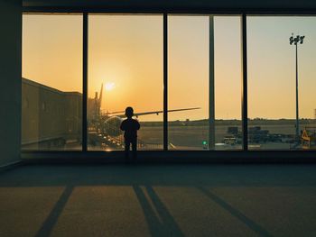 Child standing at airport departure area during sunset