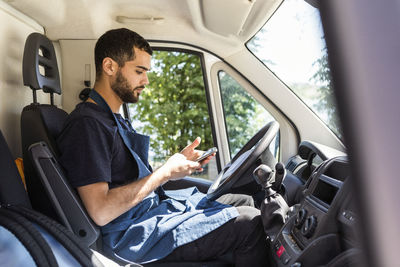 Side view of young male owner text messaging while sitting in food truck