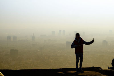 Full length of man standing on building terrace against cityscape