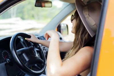 Side view of female traveler sitting on driver seat in van and enjoying road trip in summer