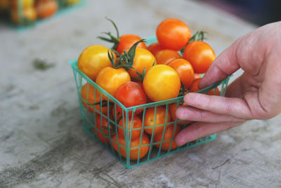 Cropped image of hand holding cherry tomatoes in container