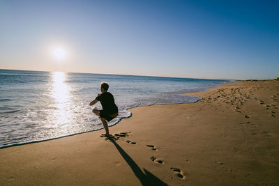 Rear view of man standing on beach against clear sky