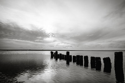 Silhouette wooden posts in sea against sky