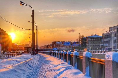 Snow covered city against sky during sunset