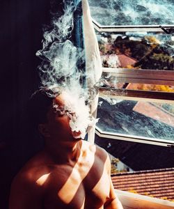 Close-up of man smoking against window