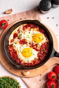 Flat lay image of shakshouka in a pan on a light coloured background close up