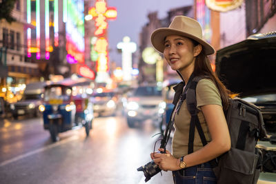 Woman standing by illuminated street in city at night