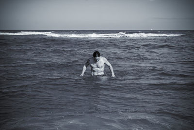 Shirtless man in sea against sky