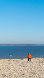 Rear view of man walking on beach against clear blue sky