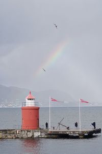 Seagulls flying over lighthouse at sea against sky