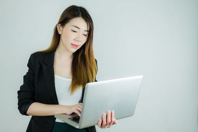 Young woman using phone while standing against white background