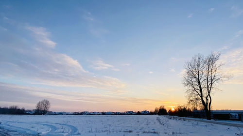 Snow covered field against sky during sunset